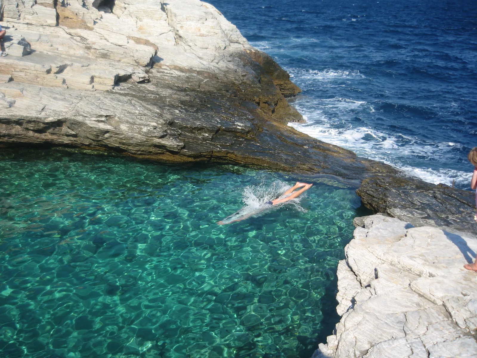 A swimmer diving into the clear water of Giola natural rock pool on Thassos